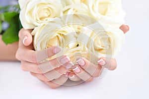 Hands of a woman with beautiful french manicure and white roses