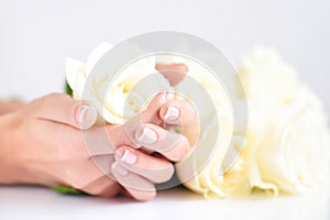 Hands of a woman with beautiful french manicure and white roses