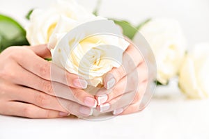 Hands of a woman with beautiful french manicure and white roses