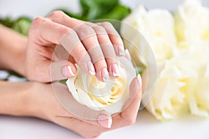 Hands of a woman with beautiful french manicure and white roses