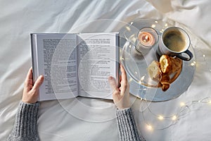 Hands of woman with book, coffee and croissants