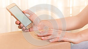 Hands of a woman with a cellphone with an empty screen and a box. Photo for online shopping. Copy space. Screen of a cellphone in
