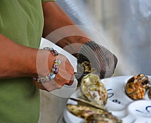 Hands of a woman with chain glove and knife opening an oyster