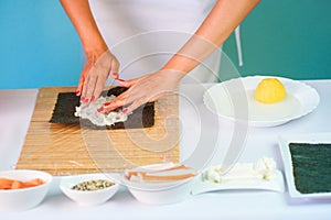 Hands of woman chef filling japanese sushi rolls with rice on a nori seaweed sheet.