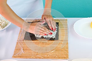 Hands of woman chef filling japanese sushi rolls with rice on a nori seaweed sheet.