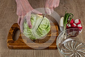 Hands of a woman chopping white cabbage with a kitchen knife on a cutting board. Preparing fresh vegan salad. Fresh vegetable