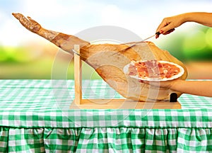 Hands of a woman cutting spanish serrano ham and presented a plate with slices of ham in front of bright soft pastel background.