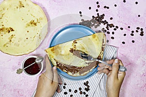 hands woman eating a Crepes stuffed with chocolate spread on blue plate with fig jam bowl and coffee beans