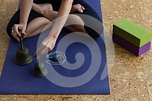 Hands of woman holding iron bells sitting on mat in lotus yoga pose