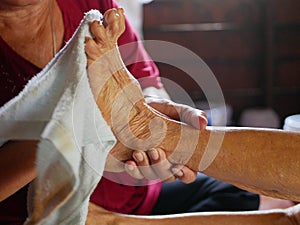 Hands of a woman holding an older person`s feet, while gently wiping / cleaning it with a wet washcloth - giving an elderly a bed