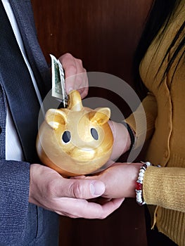 hands of woman holding a piggy bank of a golden pig and hand of man saving an american dollar bill