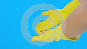 Hands of a woman housewife in yellow protective latex rubber gloves against blue background, housework and protection