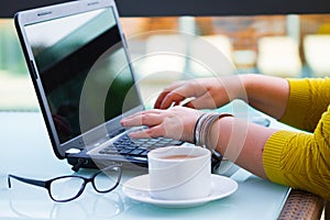 Hands of woman on the keyboard of her laptop computer. Female working on laptop in a street cafe,