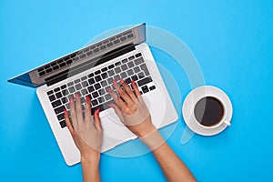 Hands of woman on a keyboard of the modern laptop over blue flat