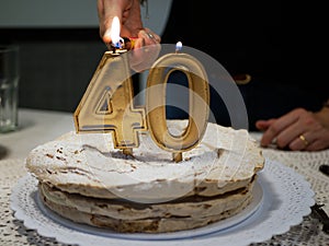 Hands of a woman lighting Golden candles four and zero of a birthday cake celebrating 40th