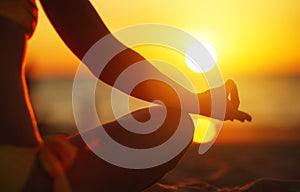 Hands of woman meditating in yoga pose at sunset on beach