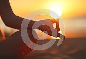 Hands of woman meditating in yoga pose at sunset on beach