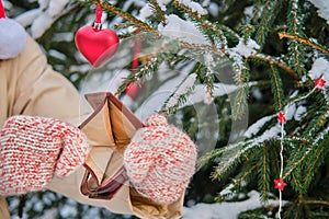 The hands of a woman in mittens hold an empty purse at the Christmas tree in a snow park on New Year`s Eve