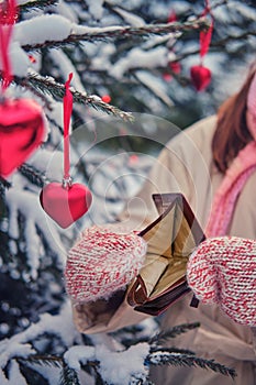 The hands of a woman in mittens hold an empty purse at the Christmas tree in a snow park on New Year`s Eve