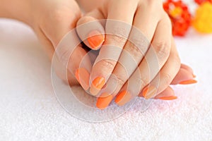 Hands of a woman with orange manicure on nails on the background of a white towel