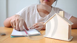 Hands of woman putting coin to House piggy bank saving money for buy home concept