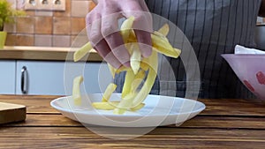 A hands of woman putting french fries on plate, slow motion