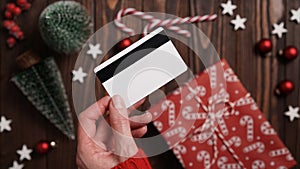 Hands of a woman in a red sweater with a credit card on a background of gift boxes, selective focus, close-up. Christmas and New