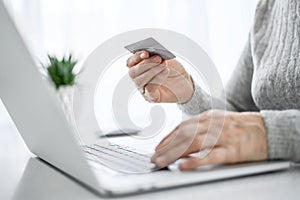 Hands of a woman senior work at a laptop with credit card using modern technology in everyday life. online shopping