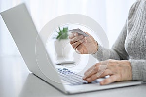 Hands of a woman senior work at a laptop with credit card using modern technology in everyday life. online shopping