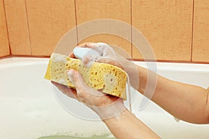 Hands of woman soaping yellow sponge in the bathroom