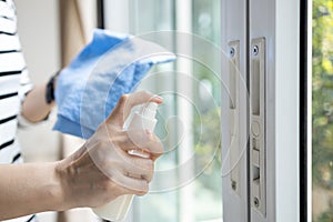 Hands of woman with spraying alcohol antiseptic,disinfecting spray,cleaning the front door,sliding glass door handle during the photo