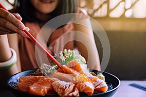 Hands woman using chopstick with raw salmon fillet and salmon roe Ikura on dish in restaurant,Japanese food