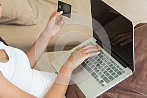The hands of woman using laptop in bed in order online with holding a credit card