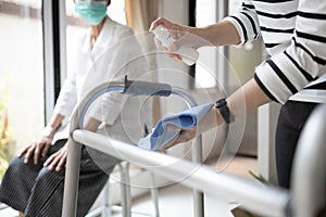 Hands of woman using spraying alcohol antiseptic,daughter is cleaning walking aids,walker for her elderly mother,during photo