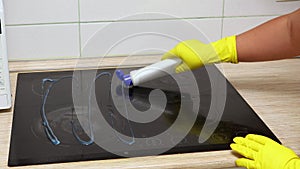 Hands of woman in yellow rubber gloves for cleaning open cap of bottle of cleaning gel for ceramic electric stove