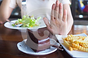 The hands of women care for health and diet, pushed from the chocolate cake and french fries plate. And choose eat vegetable or