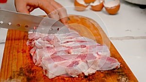 Hands of women using a knife sliced pork into pieces on cutting board in the kitchen