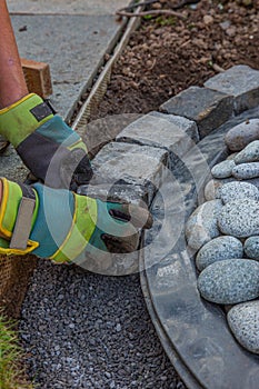 Hands with work gloves arranging gritting material and basalt cobblestones into the curb of a garden fountain