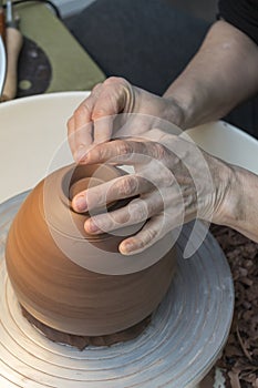 hands that work on a piece of clay that is resting on the plate of a potter's wheel
