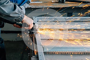 Hands of worker with close-up grinder during workflow. Man grinds grinder metal profile in shop and sparks fly