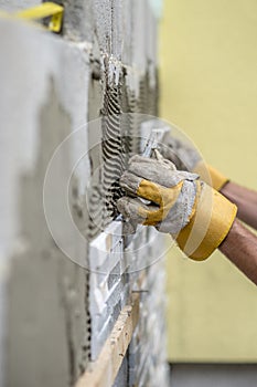 Hands of worker installing ceramic wall tiles