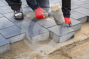 Hands of worker installing concrete paver blocks with rubber hammer
