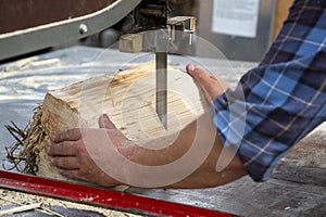 Hands of a worker sawing firewood with an industrial bandsaw