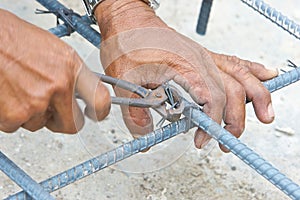 Hands of worker use pincers for knitting metal rod