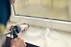 Hands of worker using a silicone tube for repairing of window photo