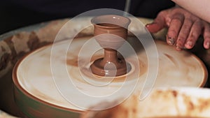 Hands working clay on potter`s wheel. Potter shapes the clay product with pottery tools on the potter`s wheel, craft factory authe