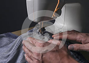 Hands working with denim cloth on sewing machine closeup. Small business concept