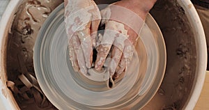 Hands working on pottery wheel with professional tools, shaping a relief on a clay plate. Top view. Potter at work