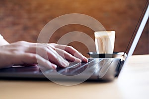 Hands working and typing on laptop keyboard with coffee cup on table in office