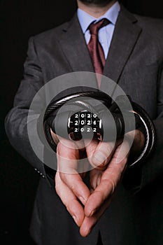 Hands wrapped with metal steel safe lock with numbers 2021 in focus  Bald man in suit out of focus. Lock down concept. Effect of